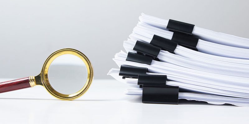 Stack of report paper documents with magnifying glass. Concept of business and search.